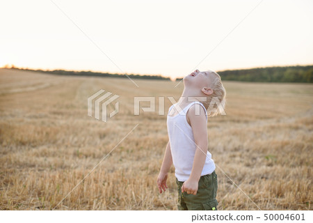 Happy blond boy stands with his head up on a mown Happy blond boy stands with his head up on a mown 50004601