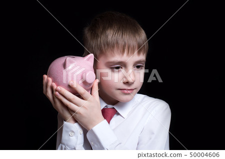 Boy listens attentively to the pink piggy bank. Boy listens attentively to the pink piggy bank. 50004606
