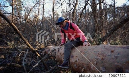 Young woman tourist with a backpack steps over a fallen tree in the forest with a backpack. Theme 50007811