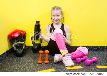 Theme sports and health children. Little Caucasian girl sits resting break floor gym holds hand Theme sports and health children. Little Caucasian girl sits resting break floor gym holds hand 50009083