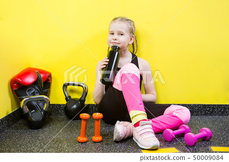 Theme sports and health children. Little Caucasian girl sits resting break floor gym holds hand Theme sports and health children. Little Caucasian girl sits resting break floor gym holds hand 50009084