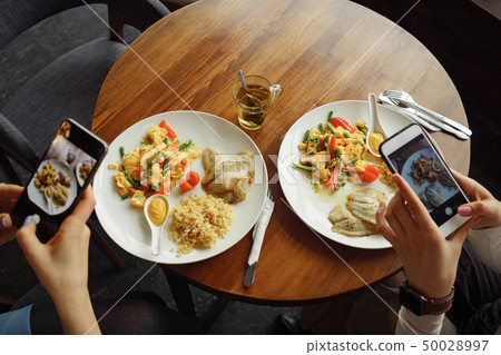 Women blogger takes pictures of her food in a cafe using mobile phone. Women blogger takes pictures of her food in a cafe using mobile phone. 50028997