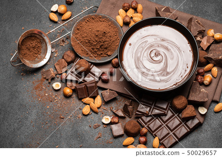 ceramic bowl of chocolate cream or melted chocolate, nuts and pieces of chocolate on dark concrete 50029657