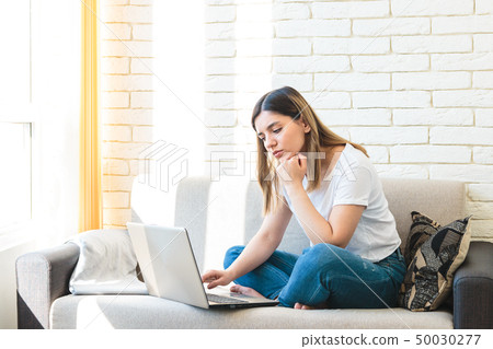 Bored young woman lying on sofa in front of laptop and yawning. Attractive lady boring because of 50030277