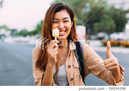 Young woman showing thumbs up with popsicle ice cream in outdoor scene 50034396