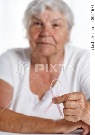 Elder woman holding pink breast cancer awareness ribbon in hand 50034671