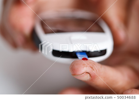 Hands of elder diabetic woman measuring blood sugar with portable pocket glucometer 50034688