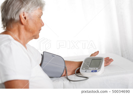 Elder woman measuring blood pressure with automatic manometer at home 50034690