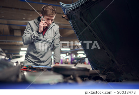 Male talking on phone standing by car with open hood. Male talking on phone standing by car with open hood. 50038478