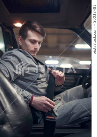 Side photo of man driver fastening seat belt while sitting in car on underground insurance Side photo of man driver fastening seat belt while sitting in car on underground insurance 50038483