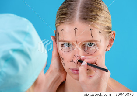 Beautician draw correction lines on woman face. Before plastic surgery operetion. Isolated on blue 50040876