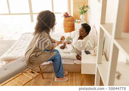 Caring nurse feeding patient lying in bed after surgery 50044778