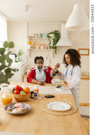 Nurse in white jacket coming to kitchen and measuring blood pressure Nurse in white jacket coming to kitchen and measuring blood pressure 50044933