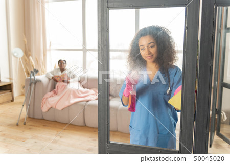 Nurse cleaning the glass door in the living room of patient Nurse cleaning the glass door in the living room of patient 50045020