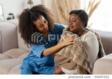 Caring curly nurse giving warm plaid to patient after catching cold Caring curly nurse giving warm plaid to patient after catching cold 50045302