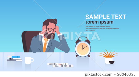 tired businessman holding head by two hands business man sitting workplace desk with alarm clock tired businessman holding head by two hands business man sitting workplace desk with alarm clock 50046353