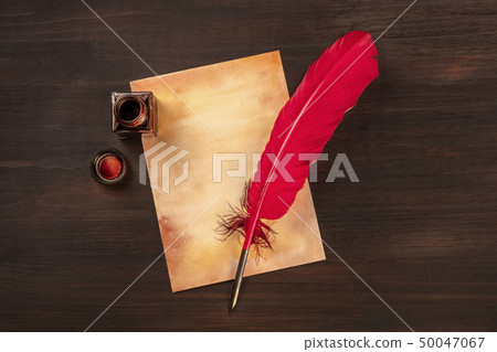 A vintage background with a vibrant red quill on a piece of old paper, with an ink well, on a dark 50047067
