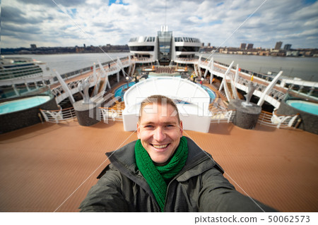 Young man makes selfie with huge cruise ship and city on background. Concept of happy vacation and Young man makes selfie with huge cruise ship and city on background. Concept of happy vacation and 50062573