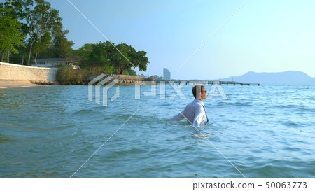 happy businessman in a suit and dark glasses is splashing in the sea at luxury resorts. concept of happy businessman in a suit and dark glasses is splashing in the sea at luxury resorts. concept of 50063773