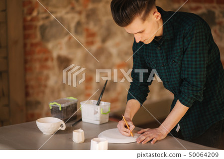 Potter making ornament on ceramic plate. Professional male potter draw a pencil on ceramic product 50064209
