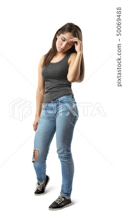 Young woman in sleeveless gray top and blue jeans standing and looking down with hand raised to 50069488