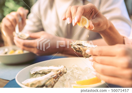 Girl with nude nails dripping lemon juice on opened oyster 50071457