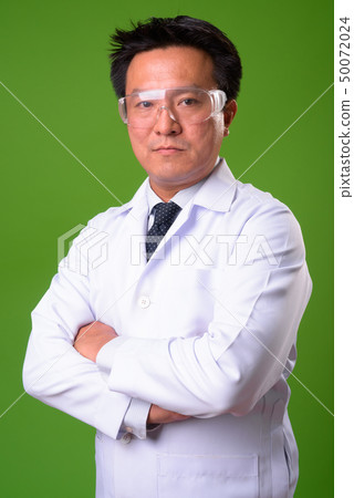 Mature Japanese man doctor wearing protective glasses against green background 50072024