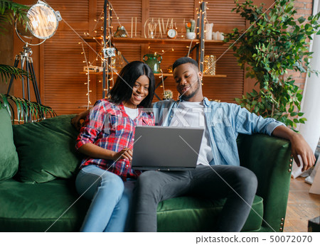 Black couple sitting on sofa and looking on laptop 50072070