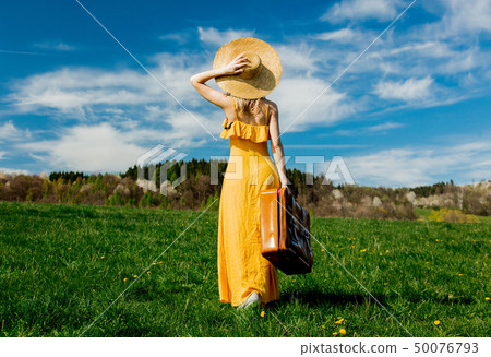 girl in yellow dress and suitcase on mountain meadow with dandelions 50076793