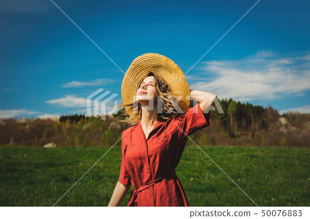 Beautiful girl in red dress and hat have a carefree time on meadow 50076883