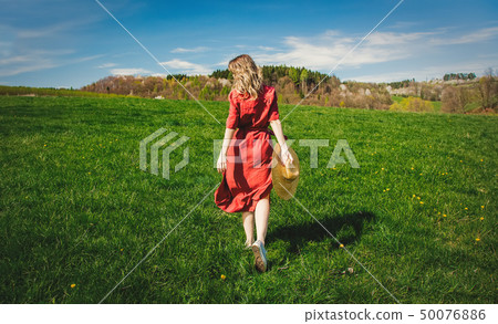 Beautiful girl in red dress and hat have a carefree time on meadow 50076886