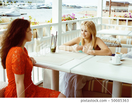 portrait of two pretty modern girl friends in cafe open air interior drinking and talking, having portrait of two pretty modern girl friends in cafe open air interior drinking and talking, having 50085363