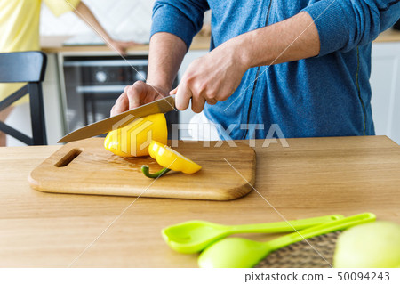 A young boy slicing yellow pepper on a wooden salad board. Cooking 50094243