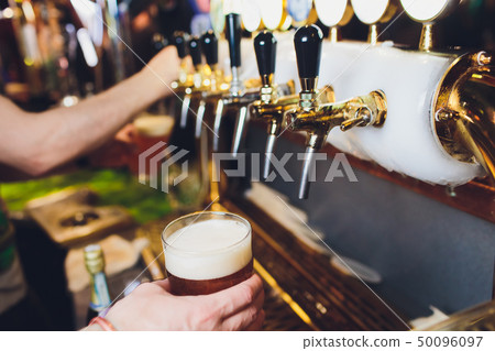 We meet oktoberfest. Hand of bartender pouring a large lager beer in tap. Pouring beer for client We meet oktoberfest. Hand of bartender pouring a large lager beer in tap. Pouring beer for client 50096097