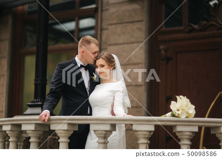 Beautiful wedding couple stand on the balcony. Stylish bride and groom in autumn weather outside Beautiful wedding couple stand on the balcony. Stylish bride and groom in autumn weather outside 50098586