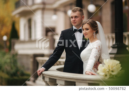Beautiful wedding couple stand on the balcony. Stylish bride and groom in autumn weather outside Beautiful wedding couple stand on the balcony. Stylish bride and groom in autumn weather outside 50098782