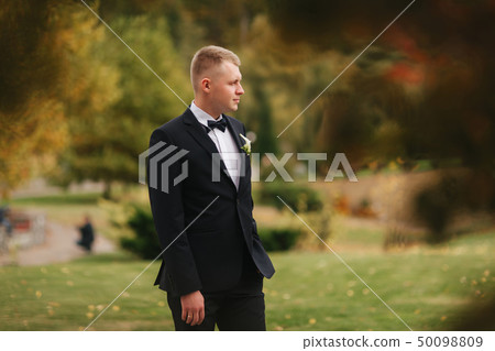 Handsome man in black suit standing outside in autumn. Groom waiting for bride Handsome man in black suit standing outside in autumn. Groom waiting for bride 50098809