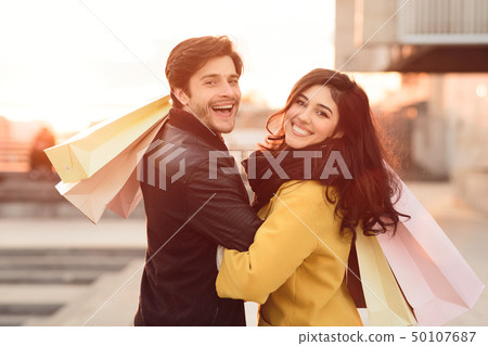 Loving couple carrying shopping bags and walking at sunset Loving couple carrying shopping bags and walking at sunset 50107687