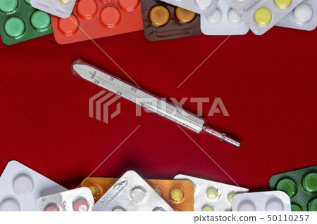 Thermometer with pills around and on a red Thermometer with pills around and on a red 50110257
