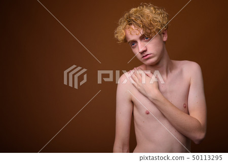 Skinny young man with curly hair shirtless against brown backgro Skinny young man with curly hair shirtless against brown backgro 50113295