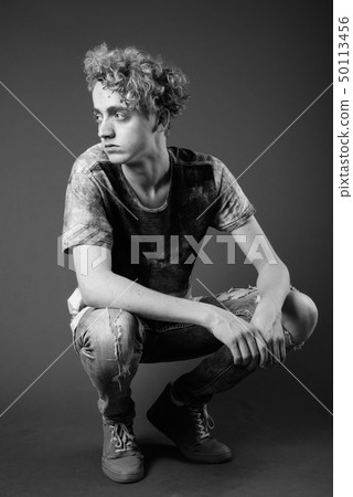 Skinny young man with curly hair against gray background in blac 50113456