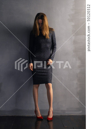 Sad girl standing near gray wall and looking down Sad girl standing near gray wall and looking down 50120312