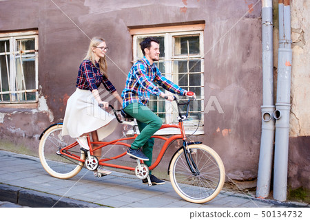 Young tourist couple, handsome man and pretty blond woman riding tandem bicycle along city street. 50134732