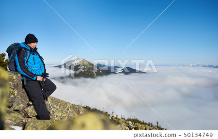 Hiker on rocky hill on background of valley with white clouds, snowy mountains and blue sky. Hiker on rocky hill on background of valley with white clouds, snowy mountains and blue sky. 50134749