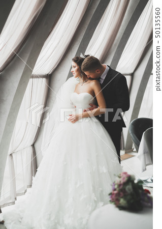 Lovely happy wedding couple, bride with long white dress posing in beautiful city Lovely happy wedding couple, bride with long white dress posing in beautiful city 50135560