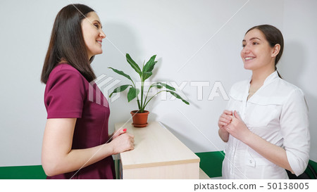 Friendly nurse on reception is talking with patient young woman, side view. 50138005