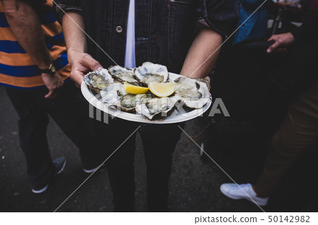 Man hand holding fresh raw oyster in paperr plate with lemon in market. 50142982