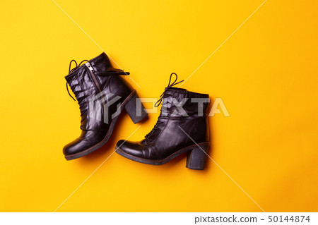 Elegant women black heeled boots. Top view of black boots on a yellow background. Elegant women black heeled boots. Top view of black boots on a yellow background. 50144874