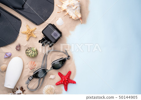 Swimming goggles, flippers, sunscreen and action camera on the sand with shells and starfishes. 50144905