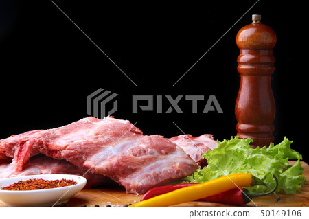 Raw Ribs on a rustic cutting board with salt, pepper and grinder for spices . Black Background for Raw Ribs on a rustic cutting board with salt, pepper and grinder for spices . Black Background for 50149106